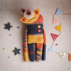 Mr. Lu-Lu crochet monster placed among colorful decor, perfect for Halloween or as a unique plush toy.