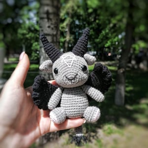 Crocheted Baphomet toy positioned on a rustic outdoor background, showcasing its black wings and mystical charm.