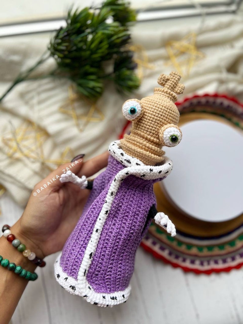 Amigurumi Kinger pattern with a purple robe and white trim, displayed in natural lighting to highlight craftsmanship.