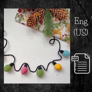 Puede incluir: Una cadena de luces de colores hecha a crochet, en tonos de verde, amarillo, rosa y azul, con un cordón negro. Las luces están dispuestas en semicírculo sobre una superficie blanca. La imagen incluye el texto "Eng (US)" y "PDF".