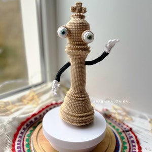 Handmade crochet Kinger toy posed on a wooden base with decorative cloth, designed for creative crochet projects.