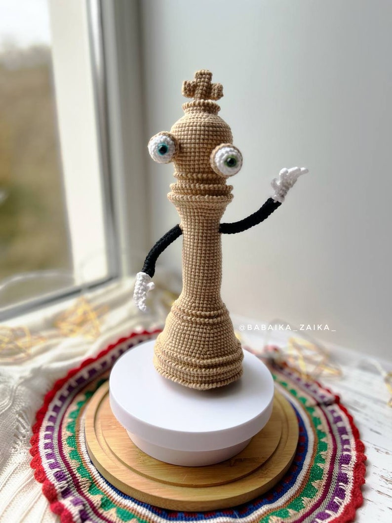 Handmade crochet Kinger toy posed on a wooden base with decorative cloth, designed for creative crochet projects.