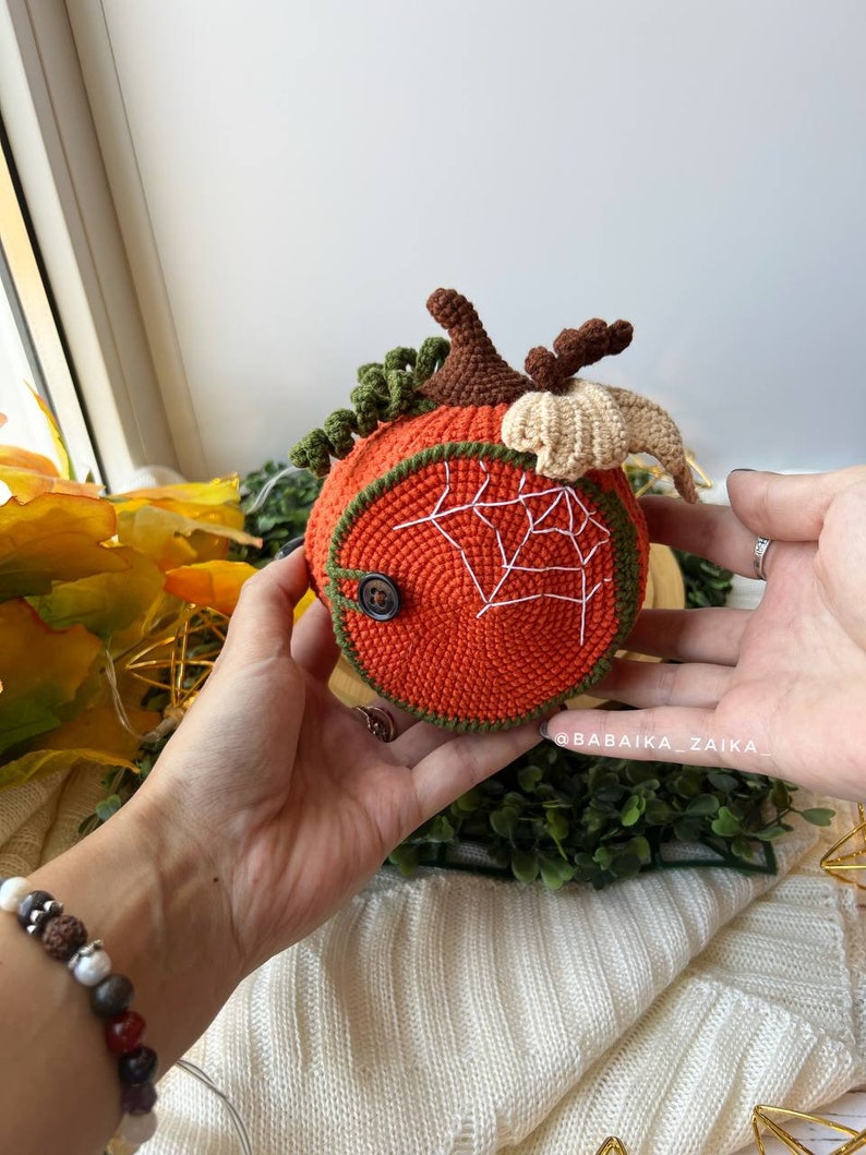 Back view of a detailed crochet pumpkin house featuring a cute spider ornament. A perfect handmade decoration for Halloween or a unique gift.
Detailed side view of an open crochet pumpkin house showcasing a handmade amigurumi spider. Unique and eco-friendly Halloween home decor.