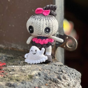 A close-up of the crochet Halloween doll being held in hand, showcasing intricate details like its stitched black eyes, tiny ghost accessory, and bow on its head. The soft yarn texture and well-crafted stitches make it an ideal handmade Halloween decoration.