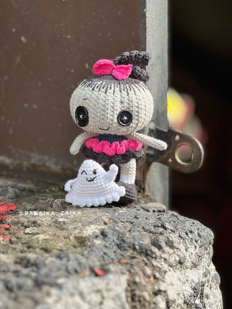 A close-up of the crochet Halloween doll being held in hand, showcasing intricate details like its stitched black eyes, tiny ghost accessory, and bow on its head. The soft yarn texture and well-crafted stitches make it an ideal handmade Halloween decoration.