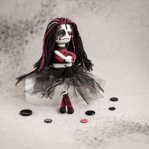 Gothic crochet doll with long black and red hair, featuring detailed stitched facial features and a dark aesthetic. Ideal for Halloween and gothic lovers.
Handmade creepy girl amigurumi doll with intricate details, dressed in black, holding a red heart. A spooky crochet pattern for horror fans.