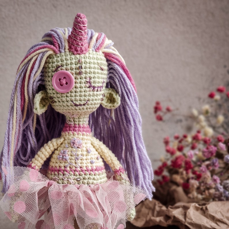 Detailed view of a handmade crochet doll with a purple and pink color scheme, designed for DIY crafting.