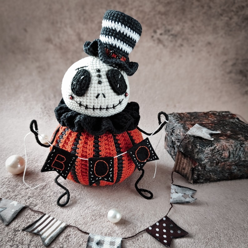 Close-up of the crochet Jack pumpkin doll, showcasing detailed stitching on the face and textured crochet patterns. The doll wears a striped top hat, adding a classic Halloween aesthetic.