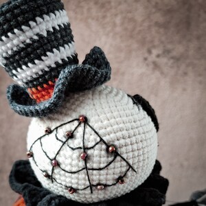 A side view of the Jack pumpkin crochet doll, emphasizing the curved, wire-like arms and puffy orange and black striped dress. The doll has a handmade, high-quality finish.