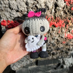 The Halloween crochet doll resting on a stone step, showcasing its balanced standing posture. The ghost in its hand adds a whimsical touch to this handmade spooky amigurumi project.