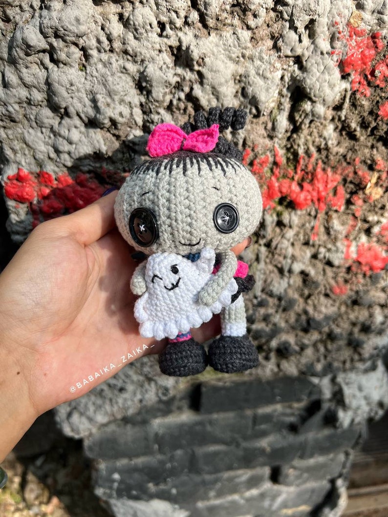 The Halloween crochet doll resting on a stone step, showcasing its balanced standing posture. The ghost in its hand adds a whimsical touch to this handmade spooky amigurumi project.