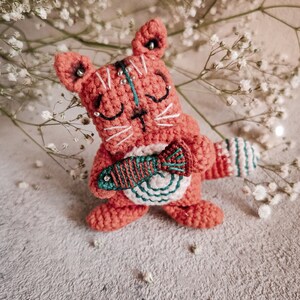The crochet kitty amigurumi is placed on brown textured paper with decorative pearls. Create your own with this easy-to-follow pattern!