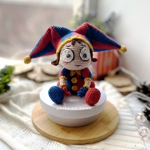 Side view of the Pomni crochet clown toy with detailed close-up on the hat's stitches and color combination. The bright crochet design makes it ideal for circus-themed decorations or unique gifts.