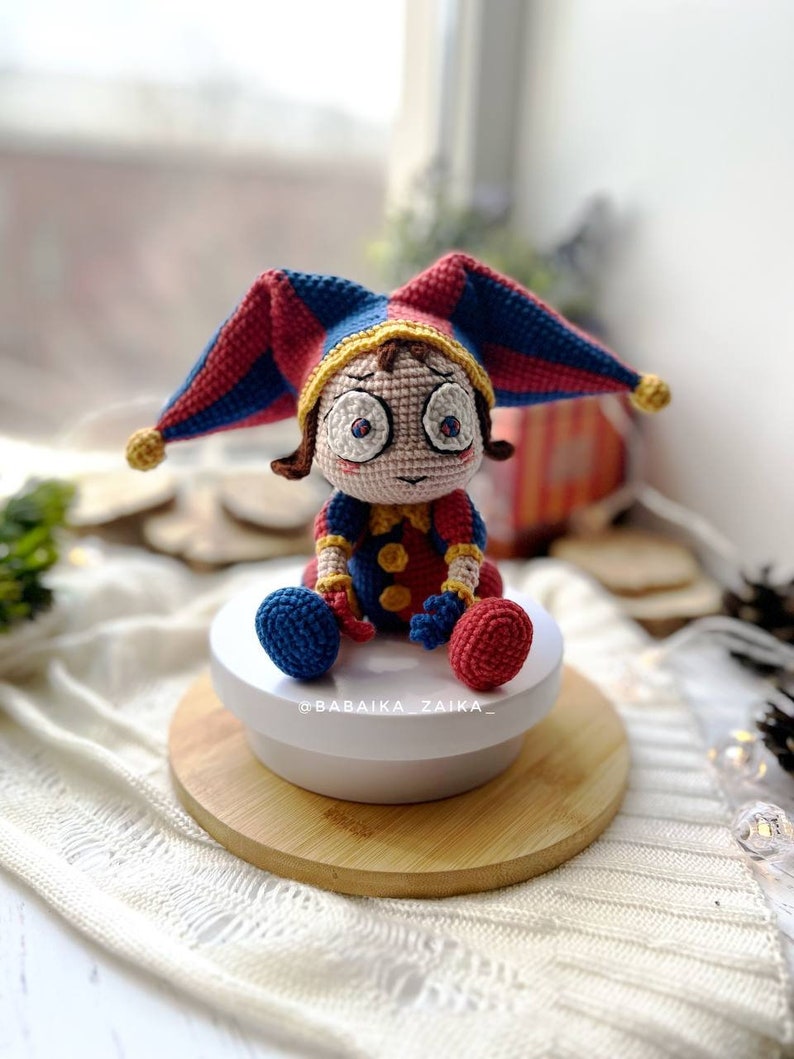 Side view of the Pomni crochet clown toy with detailed close-up on the hat's stitches and color combination. The bright crochet design makes it ideal for circus-themed decorations or unique gifts.