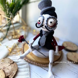 Halloween-themed crochet doll holding a red rose, seated on a wooden plate, perfect for spooky decor arrangements.
