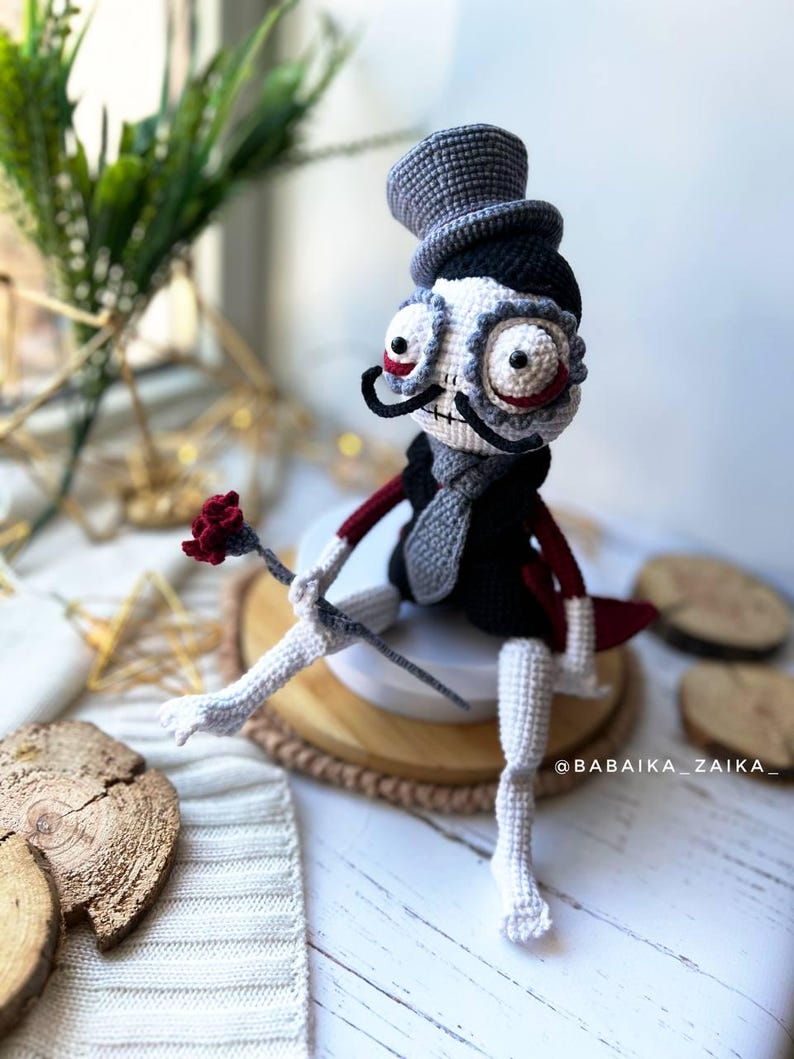 Halloween-themed crochet doll holding a red rose, seated on a wooden plate, perfect for spooky decor arrangements.