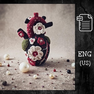 May include: A handcrafted, crocheted anatomical heart in red, black, and green, decorated with cream and red flowers. The heart is surrounded by pearls and small beads. The image includes a PDF icon and the text "ENG (US)".