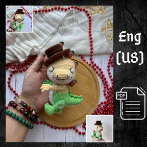 Peut inclure: Poupée reptile crochetée, avec un chapeau marron, une tête crème et un corps vert. La poupée a de petits membres et un bouton. L'image comprend un plateau en bois et des perles rouges. Le texte "Eng (us)" est visible.