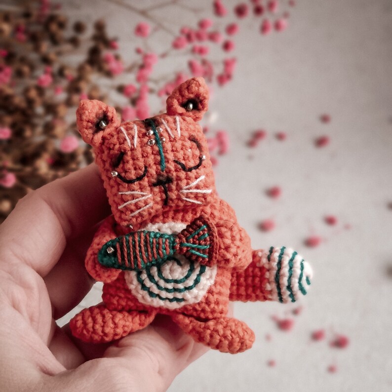 Cozy handmade amigurumi cat, sitting on textured fabric with decorative elements. A perfect crochet gift for cat lovers, made with sustainable yarn.
