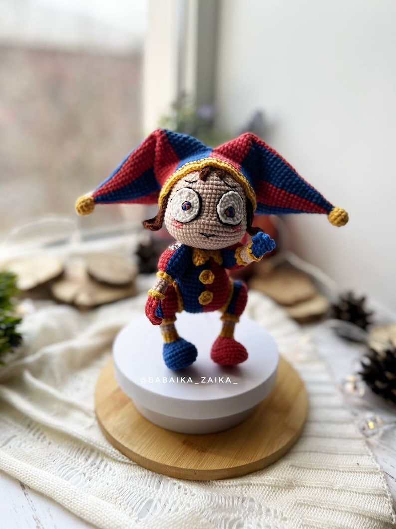 Detailed front view of the handmade crochet clown toy Pomni, emphasizing the jester hat, detailed facial expression, and high-quality crochet stitches. Ideal as a Halloween crochet decor piece.