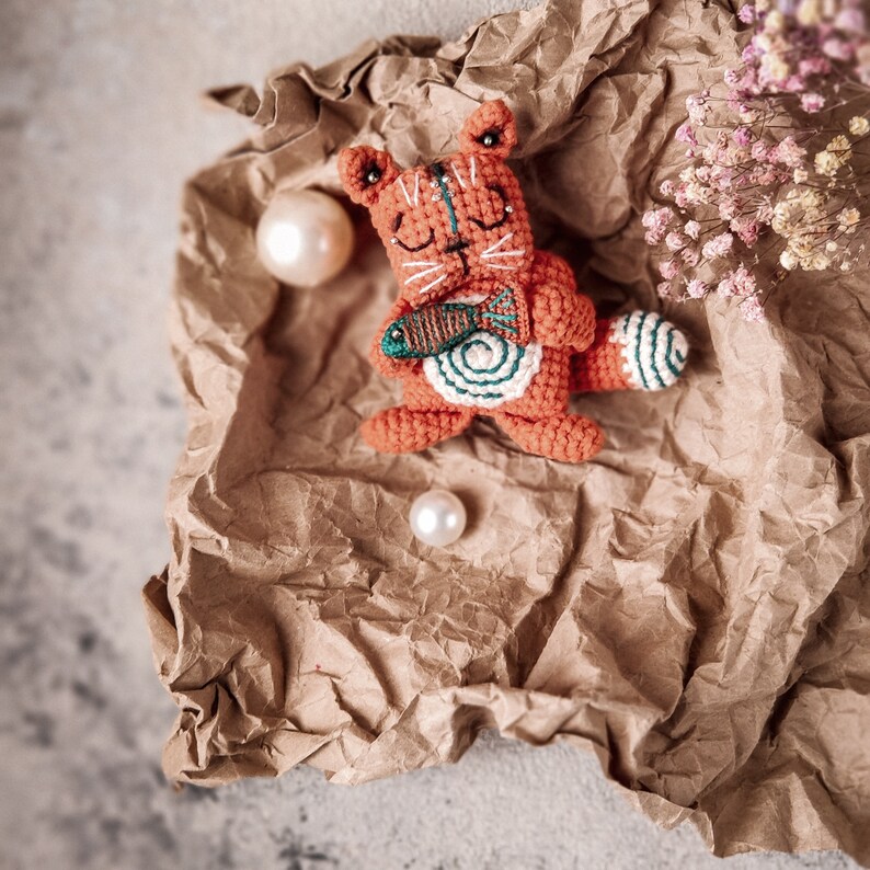 A crochet cat toy holding a fish, photographed on a rustic backdrop. This beginner-friendly amigurumi pattern is a perfect DIY craft project.