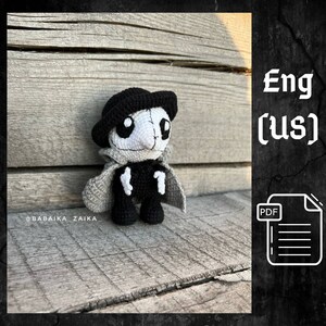 May include: A handmade crochet doll with a skeleton design. The doll is primarily black and white, with a black hat and cape. The doll is standing on a wooden surface. The text "@BABAIKA_ZAIKA" is visible.