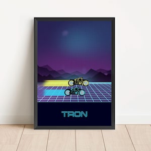 Könnte beinhalten: Ein schwarzer gerahmter Poster mit einem blauen und violetten Farbverlauf im Hintergrund. Der Poster zeigt zwei schwarze Motorräder mit leuchtenden blauen und gelben Lichtern, die auf einer Gitterbahn fahren. Der Text "TRON" ist unten auf dem Poster in Weiß gedruckt.