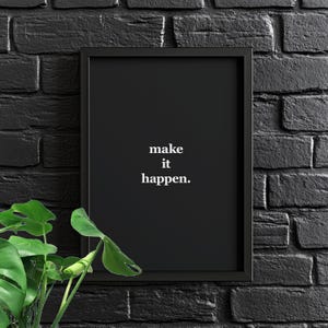 Può includere: Stampa incorniciata nera con il testo bianco "make it happen". L'opera d'arte è ambientata su un muro di mattoni neri, con fogliame verde in primo piano. Un pezzo motivazionale.