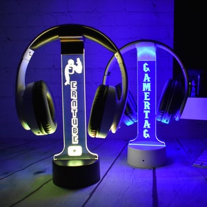 Könnte beinhalten: Zwei weiße LED-Kopfhörerständer mit individuellem Text. Der Ständer links hat den Text "EROTUBE" und ein YouTube-Logo. Der Ständer rechts hat den Text "GAMERTAG".