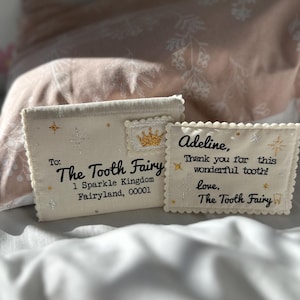 May include: Two off-white fabric envelopes with scalloped edges. The larger one reads: To: The Tooth Fairy, 1 Sparkle Kingdom, Fairyland, 00001. The smaller one reads: Adeline, Thank you for this wonderful tooth! love, The Tooth Fairy.