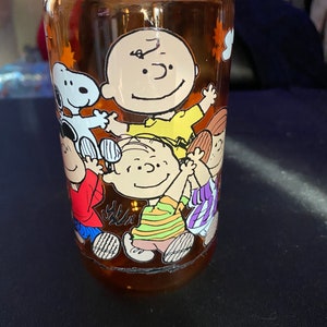 May include: An orange plastic water bottle with a Peanuts cartoon design featuring Charlie Brown, Snoopy, and other characters. The bottle has a screw-on lid.