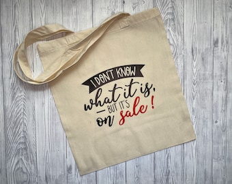 May include: A beige canvas tote bag with black and red text that reads "I don't know what it is, but it's on sale!"
