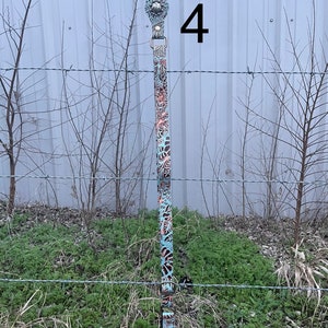 May include: A decorative leather strap with a floral pattern in shades of teal, brown, and coral. The strap has metal hardware and a clip at the top. The number "4" is visible in the image.