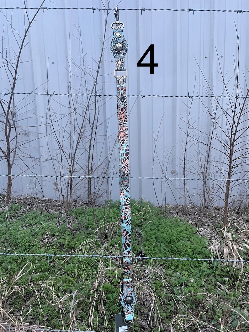 May include: A decorative leather strap with a floral pattern in shades of teal, brown, and coral. The strap has metal hardware and a clip at the top. The number "4" is visible in the image.