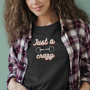 May include: A dark gray t-shirt with the text "Just a crazy" in a retro font with a white horse bit symbol in the middle.