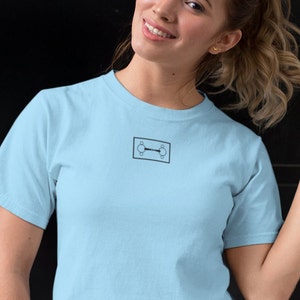 May include: A light blue t-shirt with a small black graphic of a horse bit on the front.