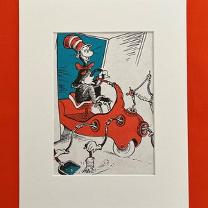 May include: A framed illustration of the Cat in the Hat driving a red vehicle. The Cat in the Hat is wearing his signature hat and bow tie. The background is a mix of blue and white. The illustration has a red border and is in a white mount.