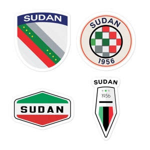 Puede incluir: Cuatro diseños de calcomanías diferentes que presentan la bandera de Sudán y la palabra "Sudán". Las calcomanías son de varias formas, incluyendo un escudo, un círculo, un hexágono y una forma puntiaguda. Las calcomanías también incluyen el año "1956" en texto blanco.