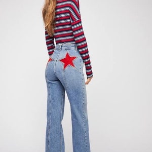 May include: A woman wearing a red, white, and blue striped long-sleeve shirt and blue denim jeans with a red star patch on the back.