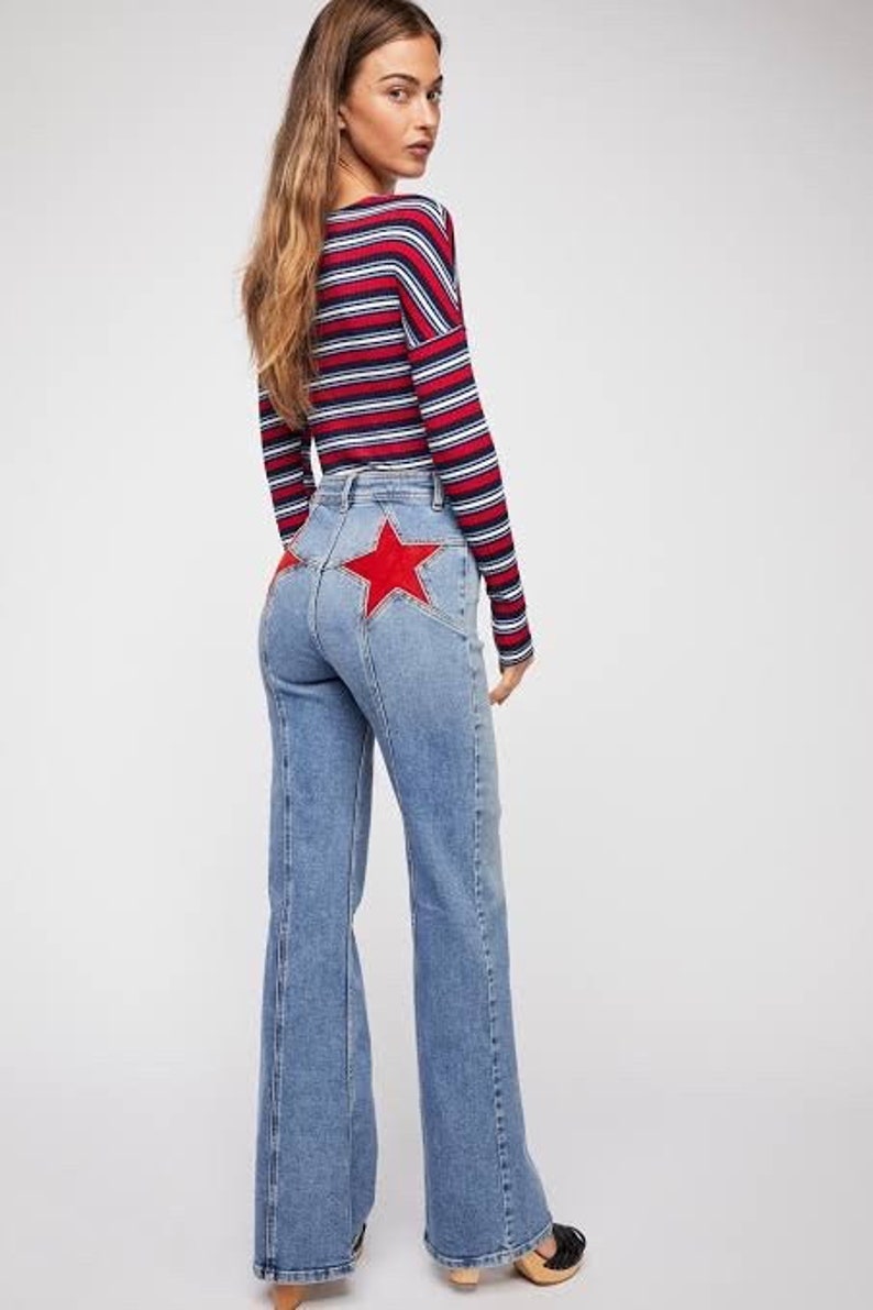 May include: A woman wearing a red, white, and blue striped long-sleeve shirt and blue denim jeans with a red star patch on the back.