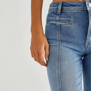 May include: Close-up of a pair of light blue denim jeans with a contrasting white seam down the front of each leg. The jeans have a high waist and a straight leg fit.