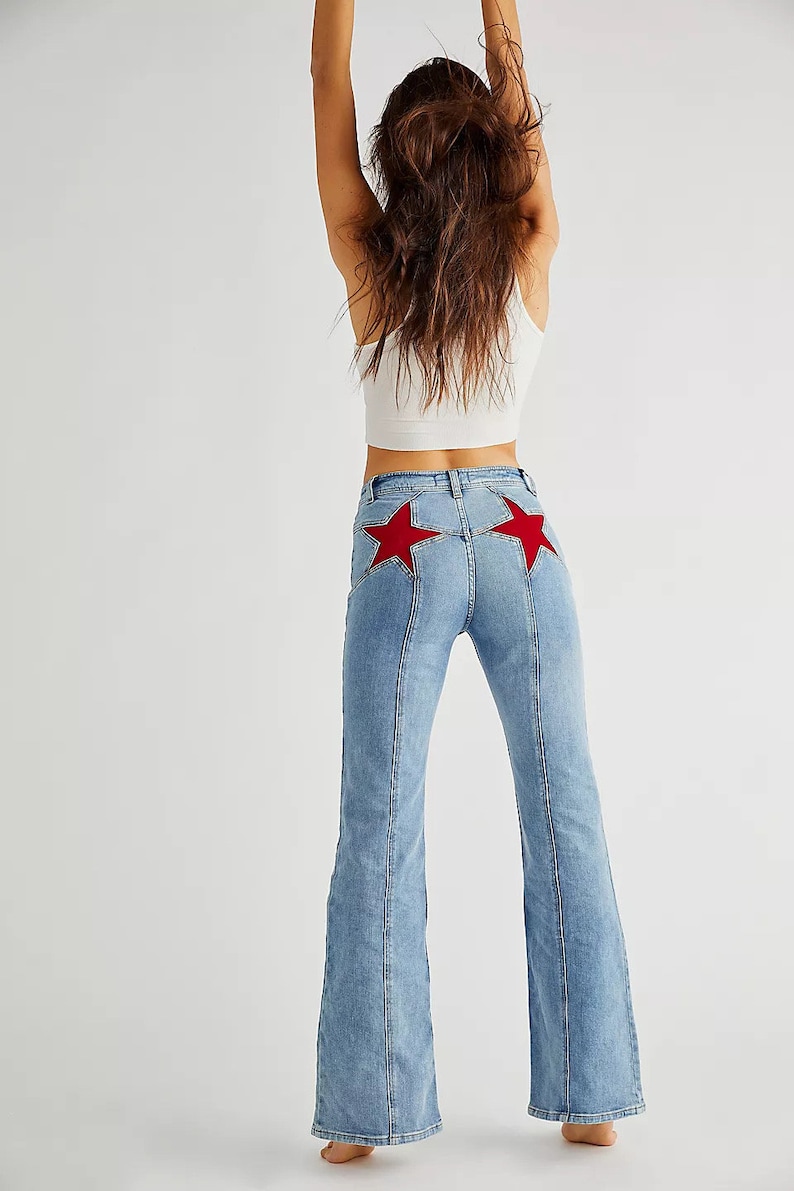 May include: A pair of light blue denim jeans with a wide leg silhouette. The jeans have a high waist and feature two red star-shaped patches on the back pockets.
