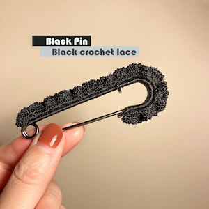 May include: Black crochet lace safety pin. The pin is made of black crochet lace and has a silver metal clasp.