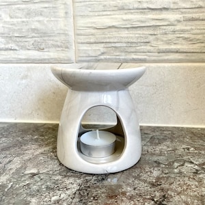 May include: A white ceramic oil burner with a marble design. The burner has a round opening in the centre to hold a tea light candle.