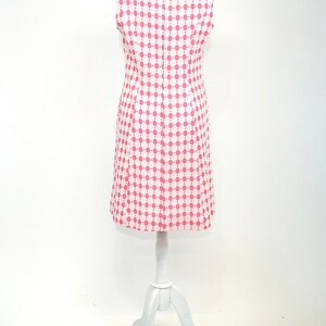 May include: A sleeveless dress with a white background and a pink geometric pattern. The dress is on a white mannequin.