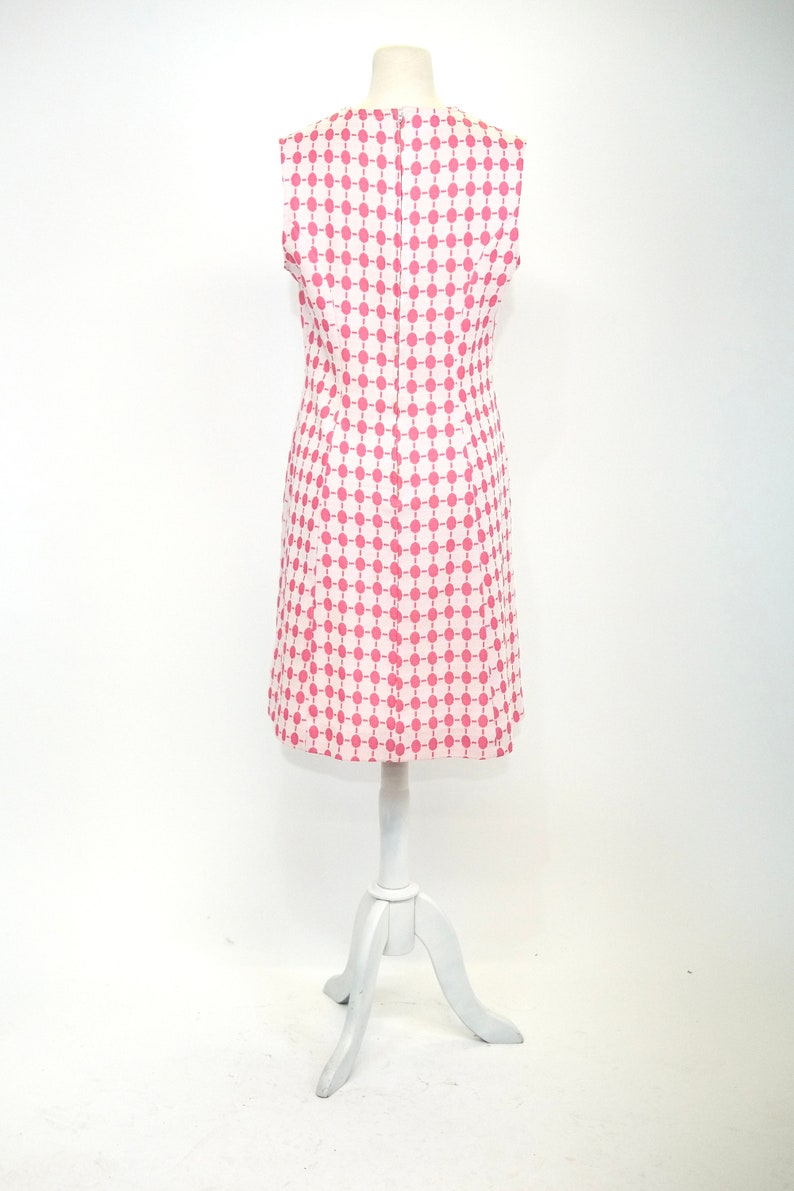May include: A sleeveless dress with a white background and a pink geometric pattern. The dress is on a white mannequin.