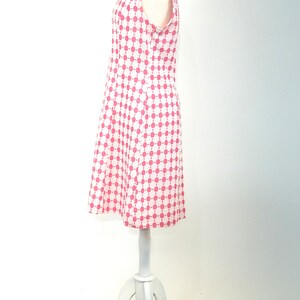 May include: A sleeveless dress with a white background and a pink geometric pattern. The dress is on a white mannequin.