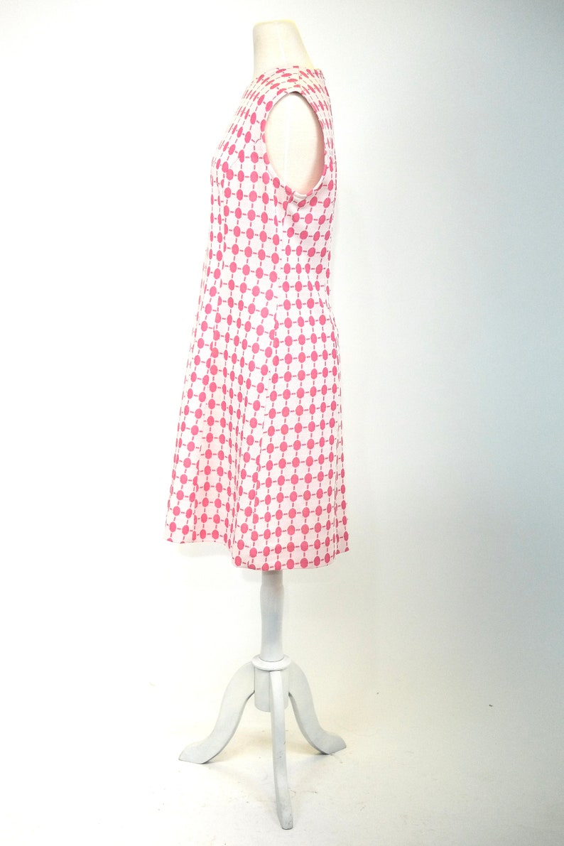 May include: A sleeveless dress with a white background and a pink geometric pattern. The dress is on a white mannequin.