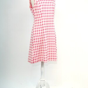 May include: A sleeveless white dress with a pink and white geometric pattern. The dress is on a white mannequin.