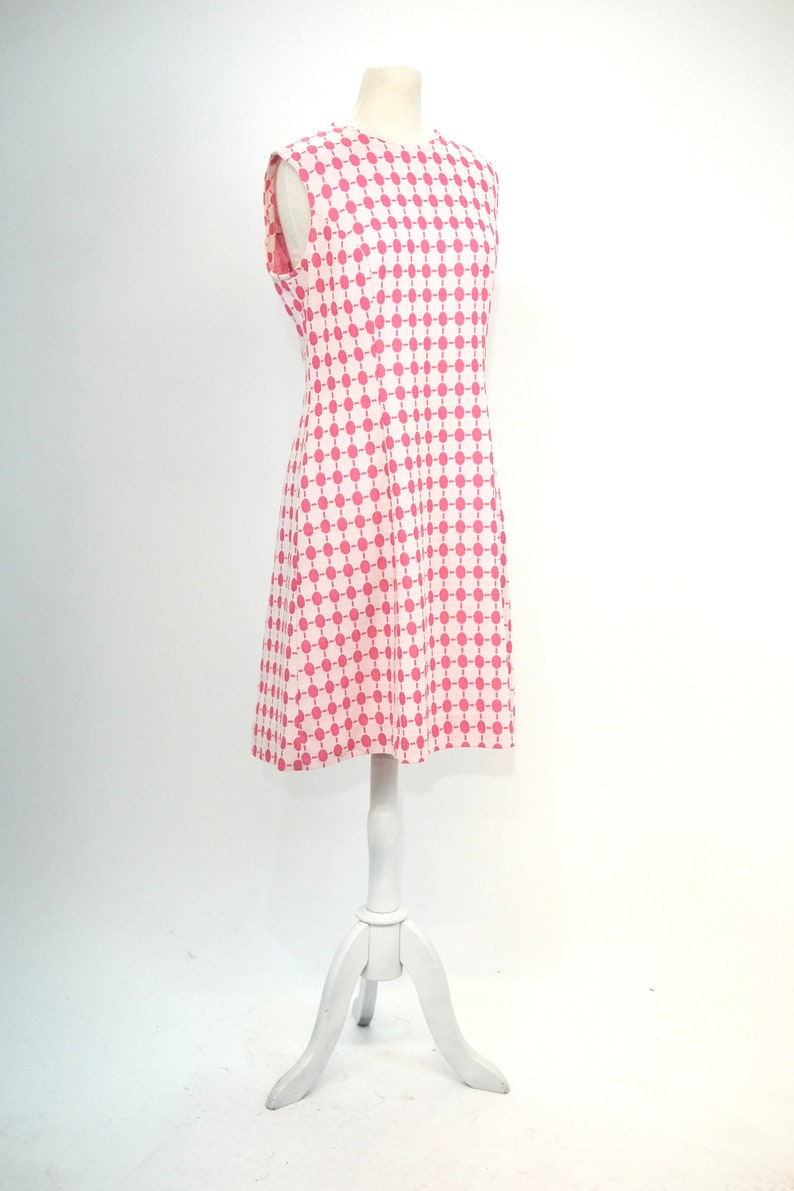 May include: A sleeveless white dress with a pink and white geometric pattern. The dress is on a white mannequin.